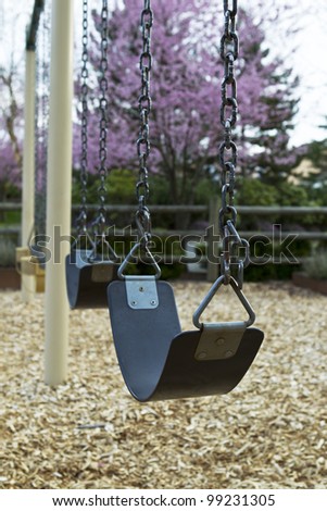 Close up of swings on empty playground with Cherry trees in background