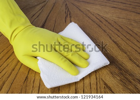 Mans hand in cleaning glove using a paper towel on a wood surface