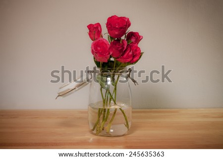 Red rose in glass canister on wooden desk top, romantic still life.