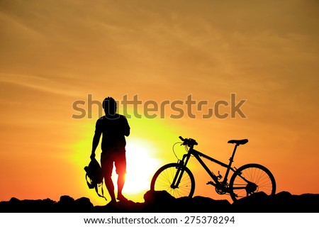 Silhouette of man and his bike on rock mountain with sunrise twilight background.