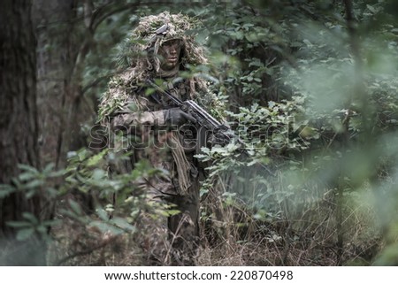 portrait of the soldier wearing ghille suit, holding assault rifle in deep forest. rifle painted camouflage. face painted camouflage.