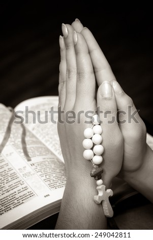 Hands folded in prayer on a Holy Bible. Black and white