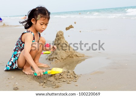 Happy asia little girl playing sand on beach with bucket and spade