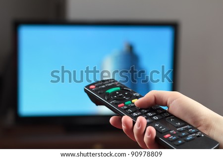 Holding TV remote control with a television as background