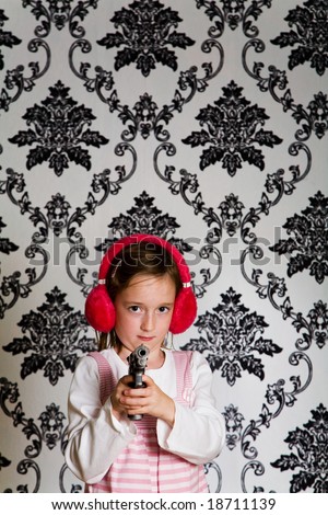 Young girl aiming a toy gun at the camera wearing red ear defenders