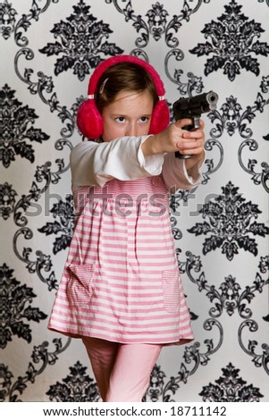 Young girl playing with a toy gun and wearing red ear defenders