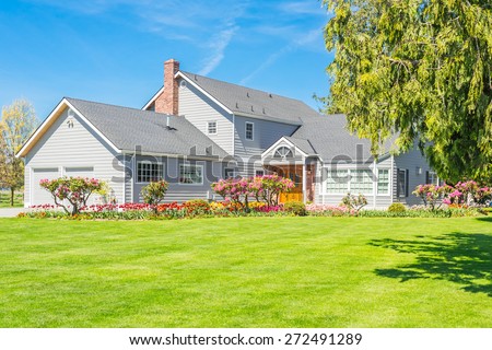 Custom built luxury farm house with nicely trimmed and designed front yard, tulips, lawn in a residential neighborhood in Canada. Large family house.