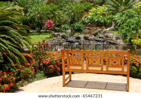 Inviting wooden bench in beautiful tropical yard with soothing water feature.