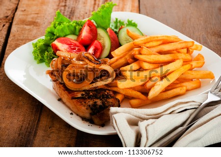 A menu with meat french potatoes roasted onion and salad on white plate