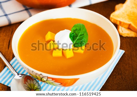 Pumpkin soup with cream in a bowl with painted flower and toast as a garnish on wood table