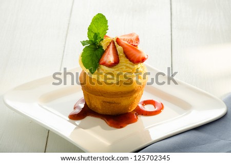 cupcake with yellow cream fresh mint leaves and strawberry as decoration strawberry sauce on the plate