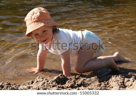 Little girl in diaper on all fours on the river coast