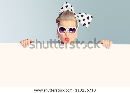 Beautiful young woman with pin-up make-up and hairstyle posing in studio with white board.