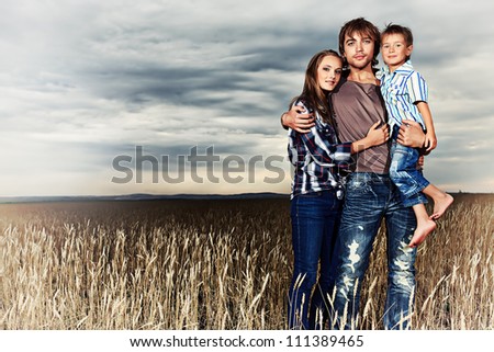 Happy family standing together in the wheat field over beautiful cloudy sky.