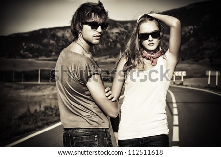 Couple of modern young people posing on a road over picturesque landscape.