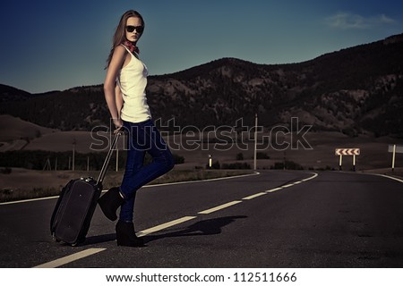 Attractive young woman hitchhiking along a road.