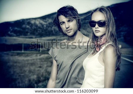 Couple of modern young people posing on a road over picturesque landscape.