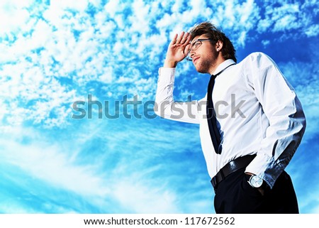 Successful business man standing over blue sky and purposefully looking away.
