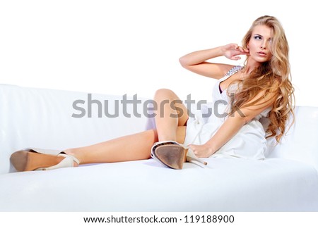 Beautiful blonde woman in light white dress sitting on a sofa. Isolated over white.