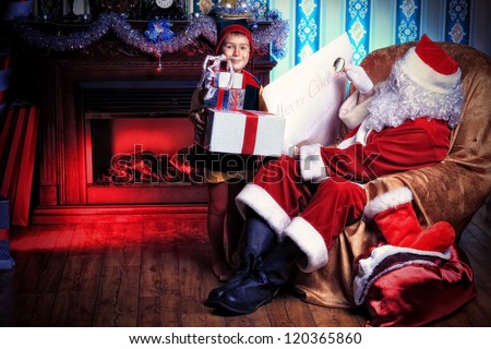 Santa Claus sitting with a little cute boy elf near the fireplace at home.