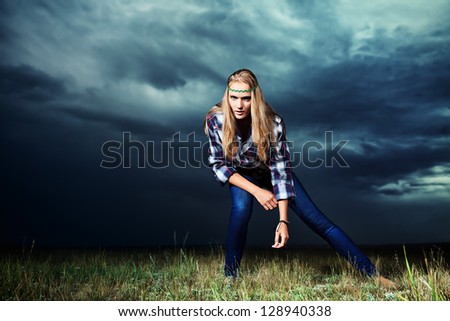 Romantic young woman in casual clothes standing in the field on a background of the storm sky.