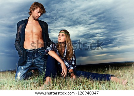 Romantic young couple in casual clothes sitting together in a field on a background of the storm sky.
