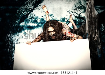 Female zombi flying at the night cemetery in the mist and moonlight and holding white board.