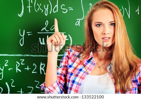 Portrait of a girl student draws attention to something important. Classroom background.