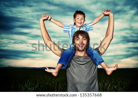Happy father holding his little son in the wheat field over beautiful cloudy sky.