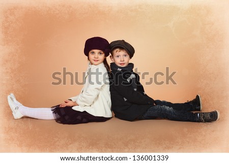 Cute little boy and girl are sitting together back to back. Retro style.