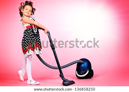 Portrait of a cute little pin-up girl with a vacuum cleaner over pink background.