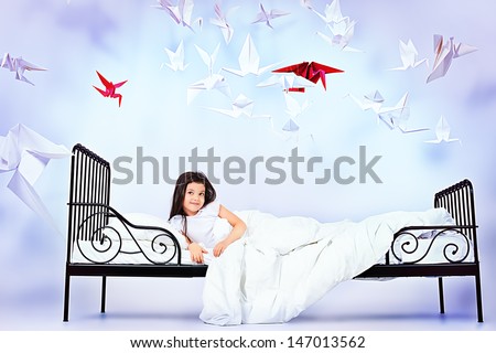 Pretty little girl lying in her bed surrounded by paper birds. Dream world.