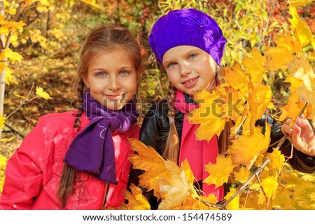 Portrait of two cute girls sisters in the leaves at the autumn park.