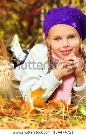 Portrait of a happy little girl lying on the leaves at the autumn park.