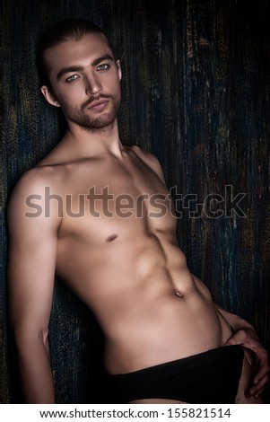 Sexual muscular nude man posing over dark background.