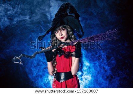 Beautiful little girl in a costume of witch posing with broom over dark background.