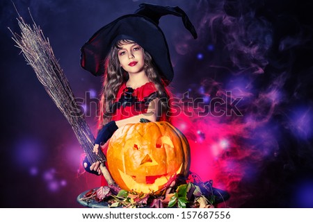 Little girl in a costume of witch posing with pumpkins over dark background.