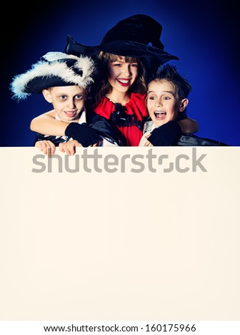 Happy children in halloween costumes posing over dark background. Copy space.