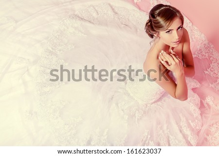Beautiful charming bride in a luxurious dress looking up. Over pink background.