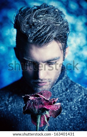 Portrait of a handsome man dressed in winter clothes, holding a rose, covered with snow.