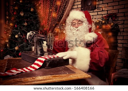 Santa Claus is sewing on a sewing machine striped socks for Christmas.