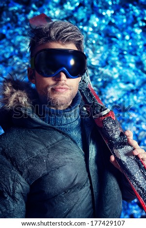 Portrait of a handsome man dressed in winter clothes, holding skiing, covered with frost.