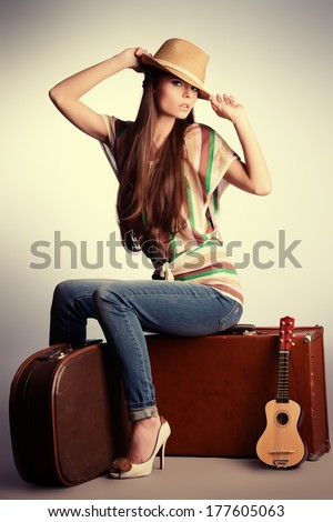 Attractive girl sitting on her old suitcases. Travel and tourism. Studio shot.
