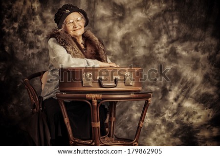 Beautiful old lady in an elegant old-fashioned clothes sitting on suitcases. Vintage style.