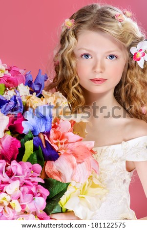 Beautiful tender girl with long curly hair holds bouquet of flowers. Over pink background.
