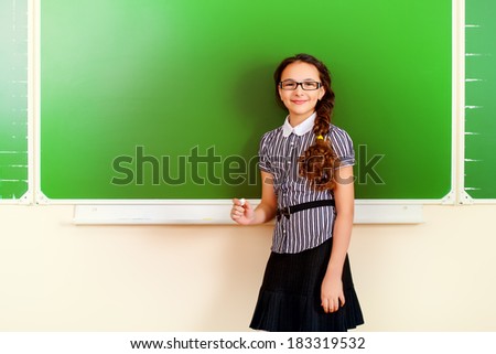 Smiling schoolgirl performs the task at the blackboard. Education.