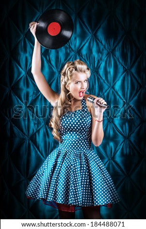 Pretty pin-up woman singing with vinyl record over vintage background.