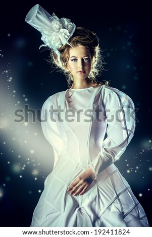 Portrait of a beautiful fashion model in the refined white dress and elegant hat. Snow queen. Winter fantasy.