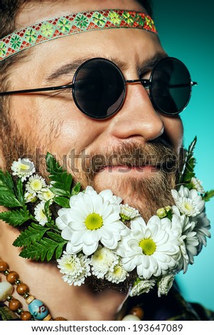 Funny smiling young man in glasses and a beard of flowers. Hippie style.