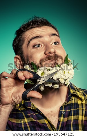 Funny and handsome young man cut his beard of flowers with scissors.